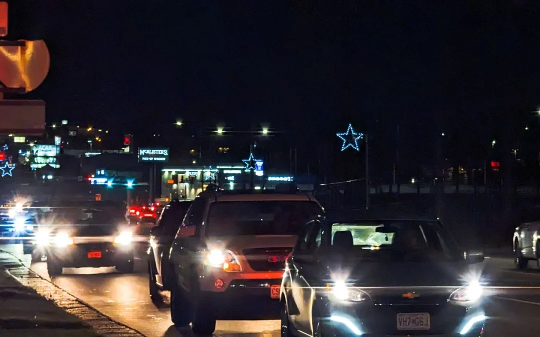 Cars driving through a city street at night with headlights and holiday lights on