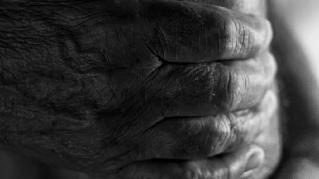 Elderly hands gripping a knee, showing joint pain linked to osteoarthritis