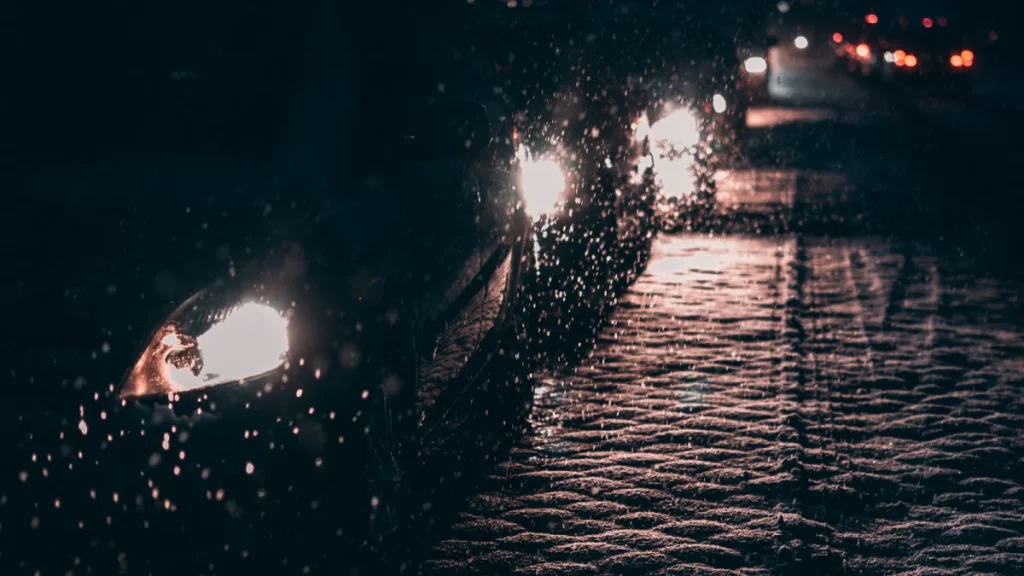 Cars in evening traffic on a wet road with headlights on after dark