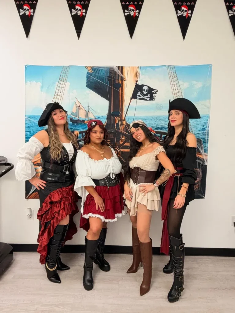 Four members of the Spine and Injury Associates Haines City staff in pirate costumes in front of a pirate ship backdrop