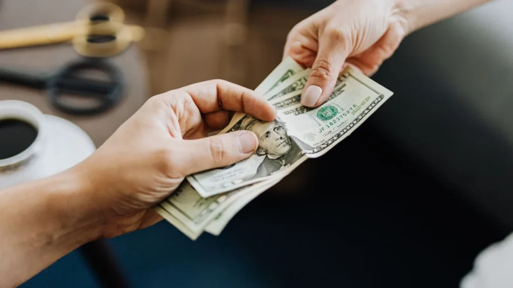 Hands holding US dollar bills, representing what chiropractors earn each year