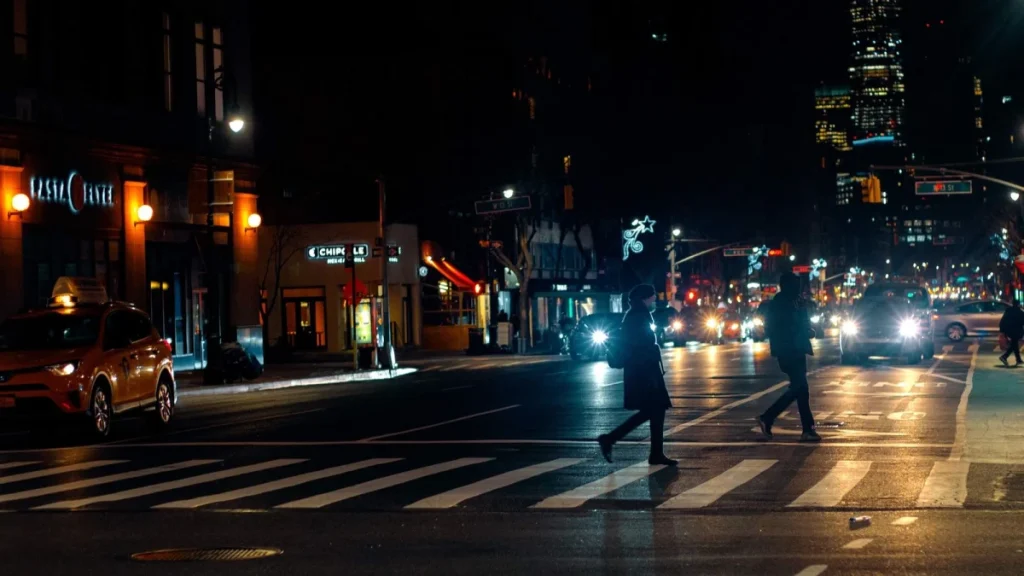 Pedestrians crossing a busy city road on an autumn evening after sunset