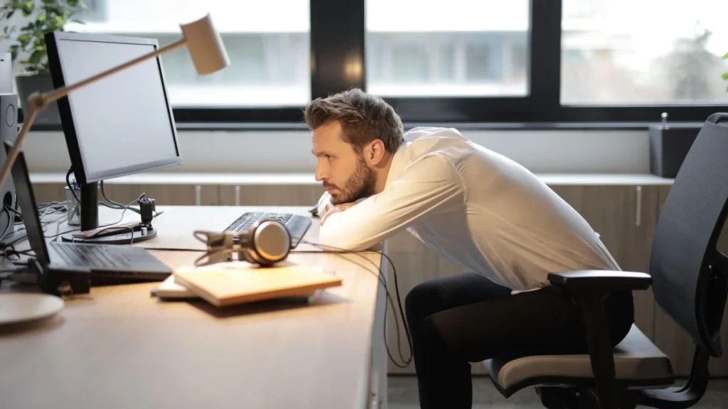 Man leaning over his office desk with poor posture that strains the back