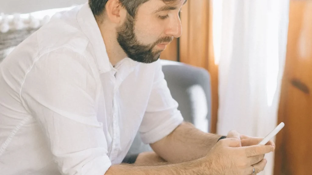 Man sitting on a sofa with his phone, a sedentary habit that hurts backs