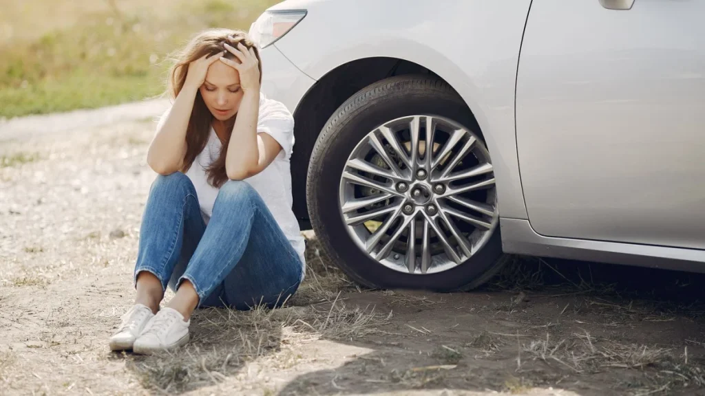 Worried woman sitting by her car, showing the stress a car accident leaves behind